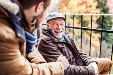 Two men engaged in conversation while seated on a balcony, enjoying a relaxed atmosphere having managed dementia behavior problems.